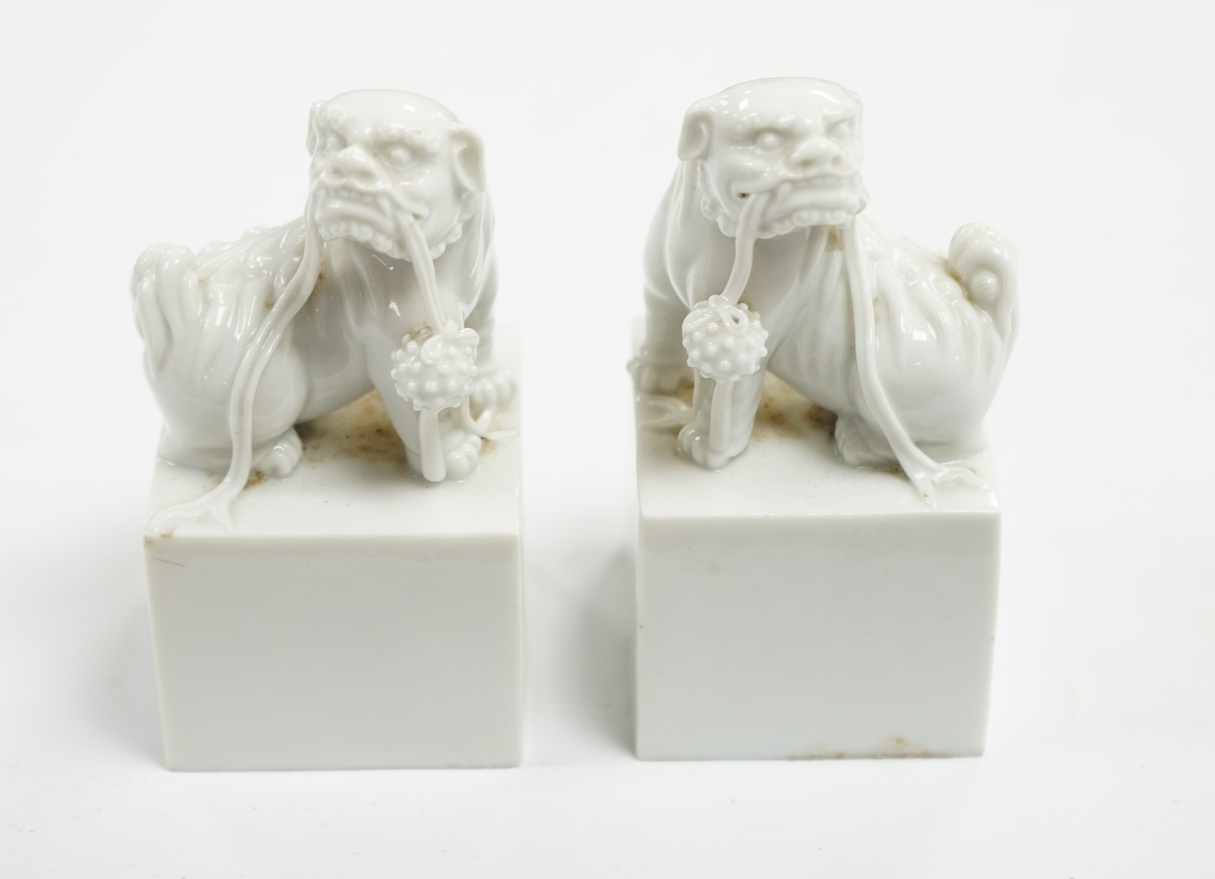 A pair of Japanese Hirado style white glazed porcelain Shishi lion-dog seals and a wooden stand, 10.5cm high. Condition - slight manufacturing glazing losses to base edges